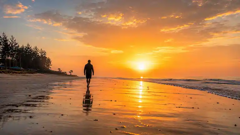Person walking along the shore during a golden sunrise at Lal Kakra Beach.