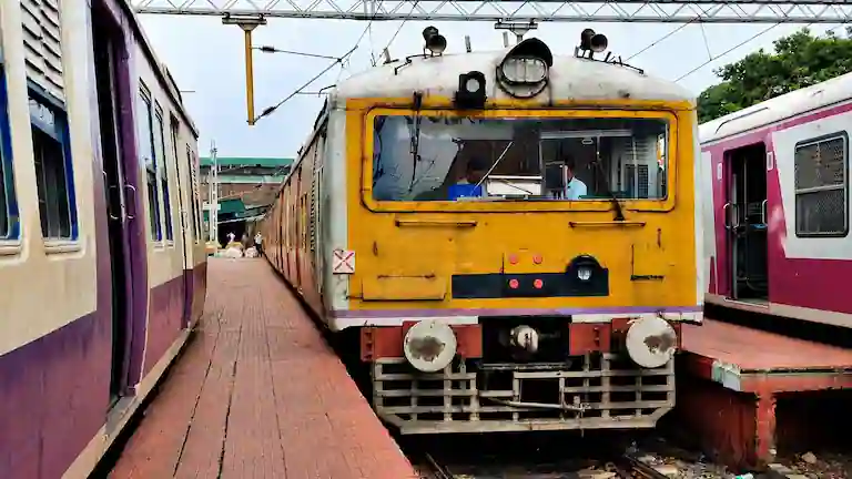 A yellow and red Sealdah South section local train standing at a railway platform.