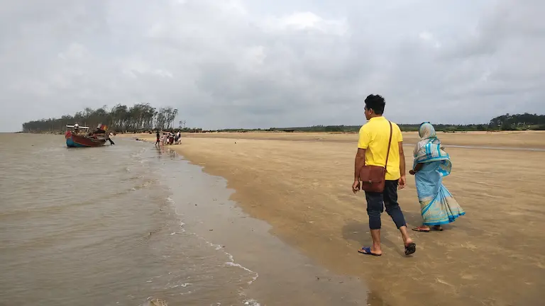 Tourists walking on the flat sand of Talsari Sea Beach during low tide.