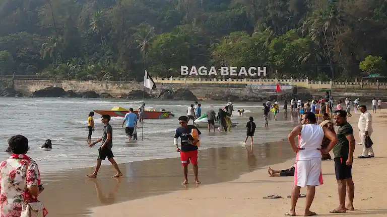Tourists standing on the crowded shoreline near the white landmark sign at Baga Beach.