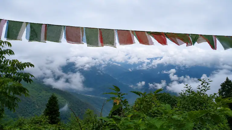 Scenic valley view of Teesta river and green mountains from Ramdhura viewpoint framed by prayer flags.