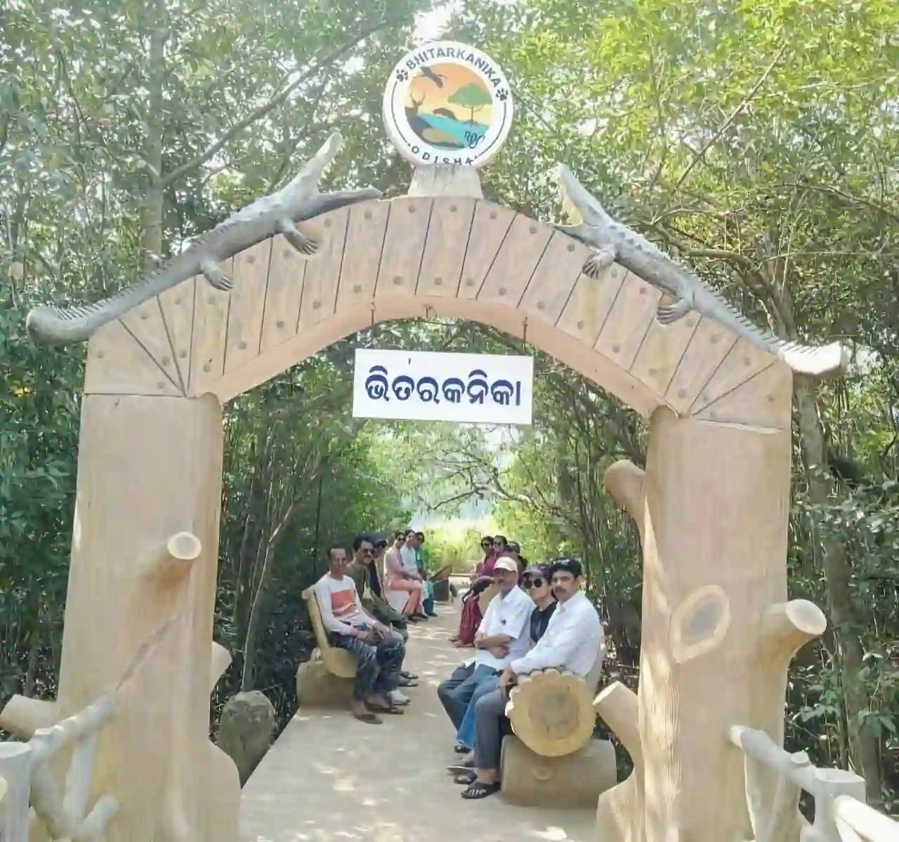 Tourists sitting under the crocodile-themed entrance archway at Bhitarkanika National Park, Odisha.