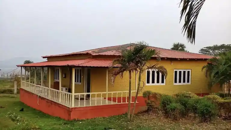 A yellow cottage-style tourist lodge with a red roof and porch near Chandipur Beach.