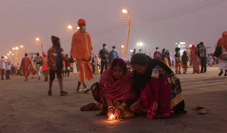 Pilgrims lighting diyas on the foggy beach during the best time to visit Gangasagar.