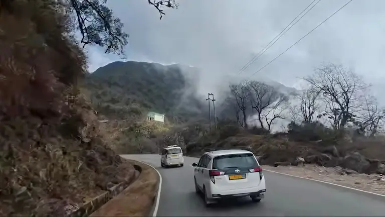 Cars navigating a steep, misty mountain road on the drive to Sikkim.