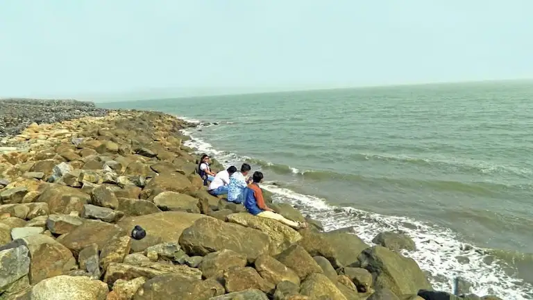Tourists sitting on the stone sea wall at Pentha Sea Beach.