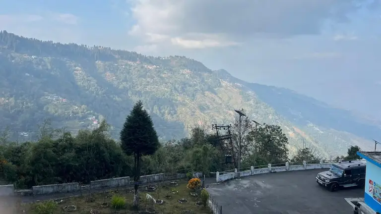 A black SUV parked at a high-elevation scenic viewpoint overlooking forested mountains on the route to Darjeeling.