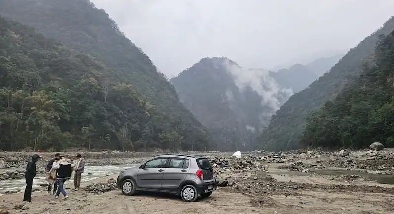 A small hatchback parked on a rocky riverbed in the mountains along the Gangtok to Darjeeling distance.