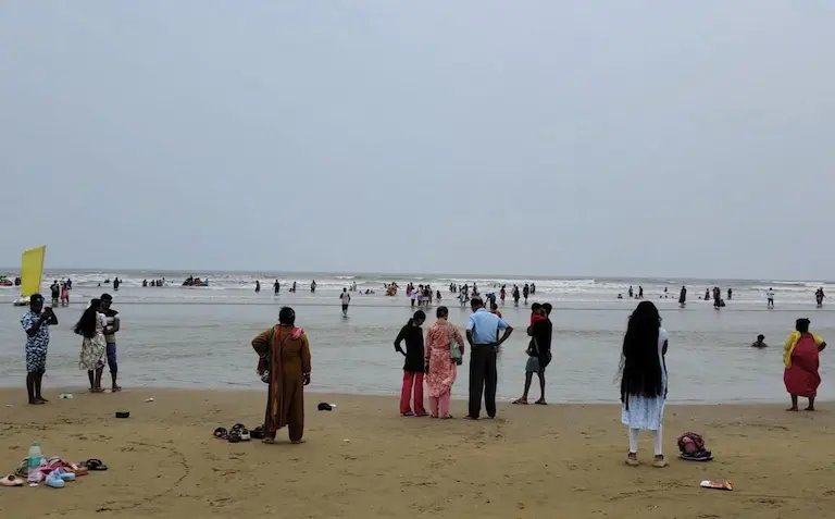 Massive crowds of tourists bathing in the muddy sea water at Udaipur Beach.