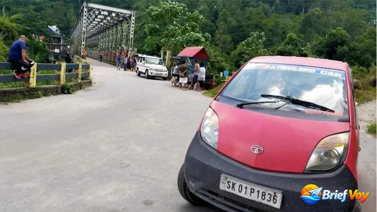 A red car parked near the long steel bridge at Jogighat on the Mungpoo route from NJP to Sittong.
