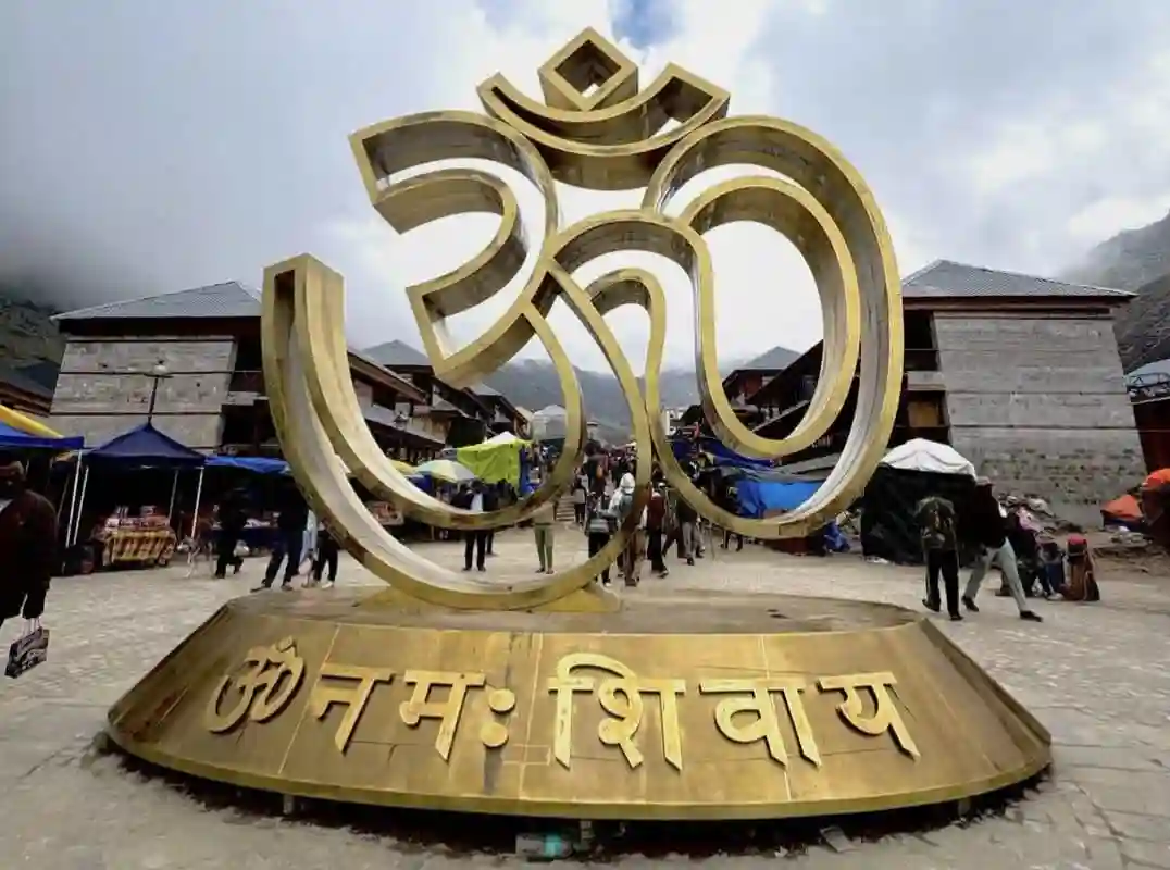 Large golden Om symbol sculpture surrounded by pilgrims arriving at the Kedarnath settlement.