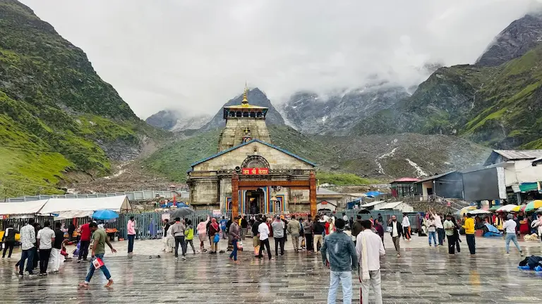 Pilgrims gathering at Kedarnath Temple in cloudy mountain weather after overcoming the high kedarnath trek difficulty level of the 16km climb.