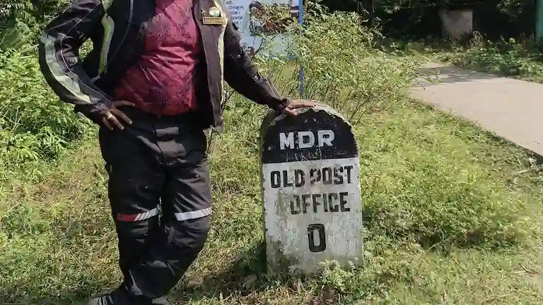 Author on a motorcycle road trip standing next to the Old Post Office milestone in Khejuri