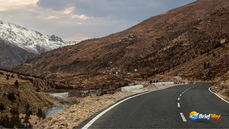 Paved mountain highway winding through Lahaul Valley Himachal Pradesh alongside a riverbed toward snow peaks