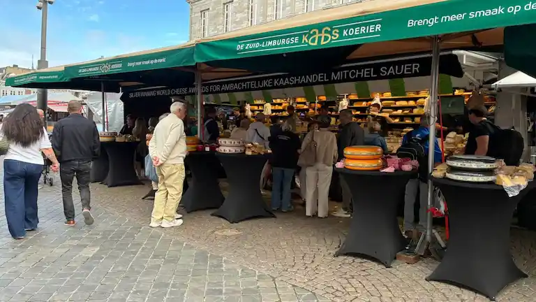 Locals gathering around a fresh cheese and food stall at the weekly outdoor Friday Market in Maastricht.