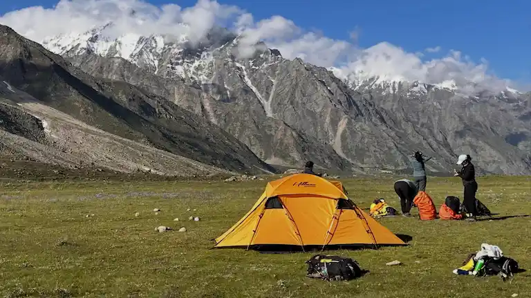 Trekkers pitching a yellow tent at a campsite on the Miyar Valley trek.