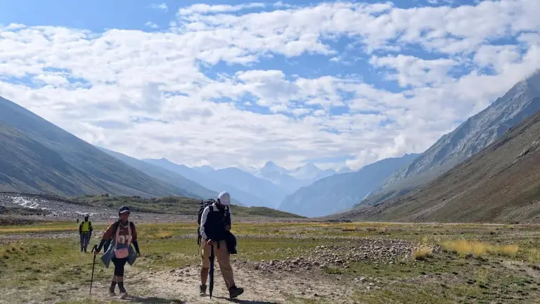Trekkers hiking across the wide, flat, and rocky landscape of the Miyar Valley.