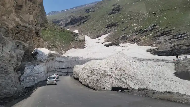 Cars driving through massive snow walls on the paved Rohtang Pass road to Lahaul Valley