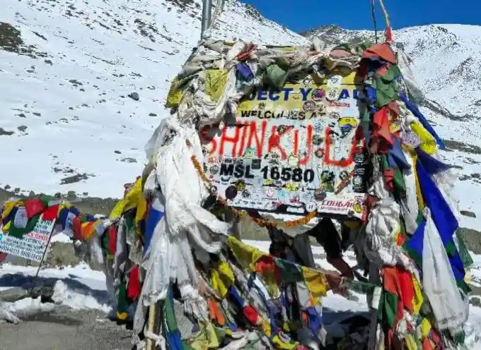 Shinkula Pass summit board covered in prayer flags showing the old 16580 feet altitude sign