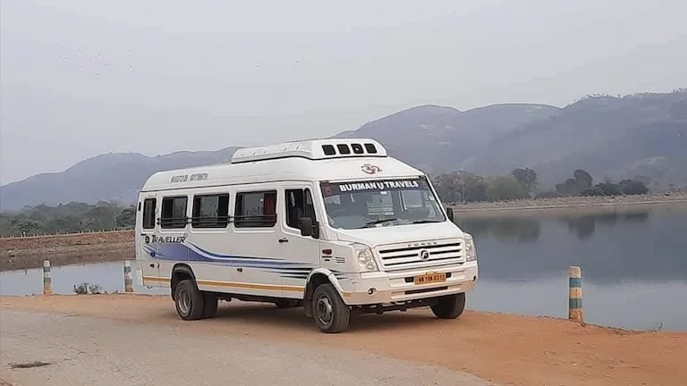 White AC Tempo Traveller Kolkata tourist vehicle with a yellow commercial plate parked near a lake.